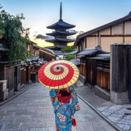 Una mujer con kimono y sombrilla roja ante la pagoda de Yasaka, en Kioto