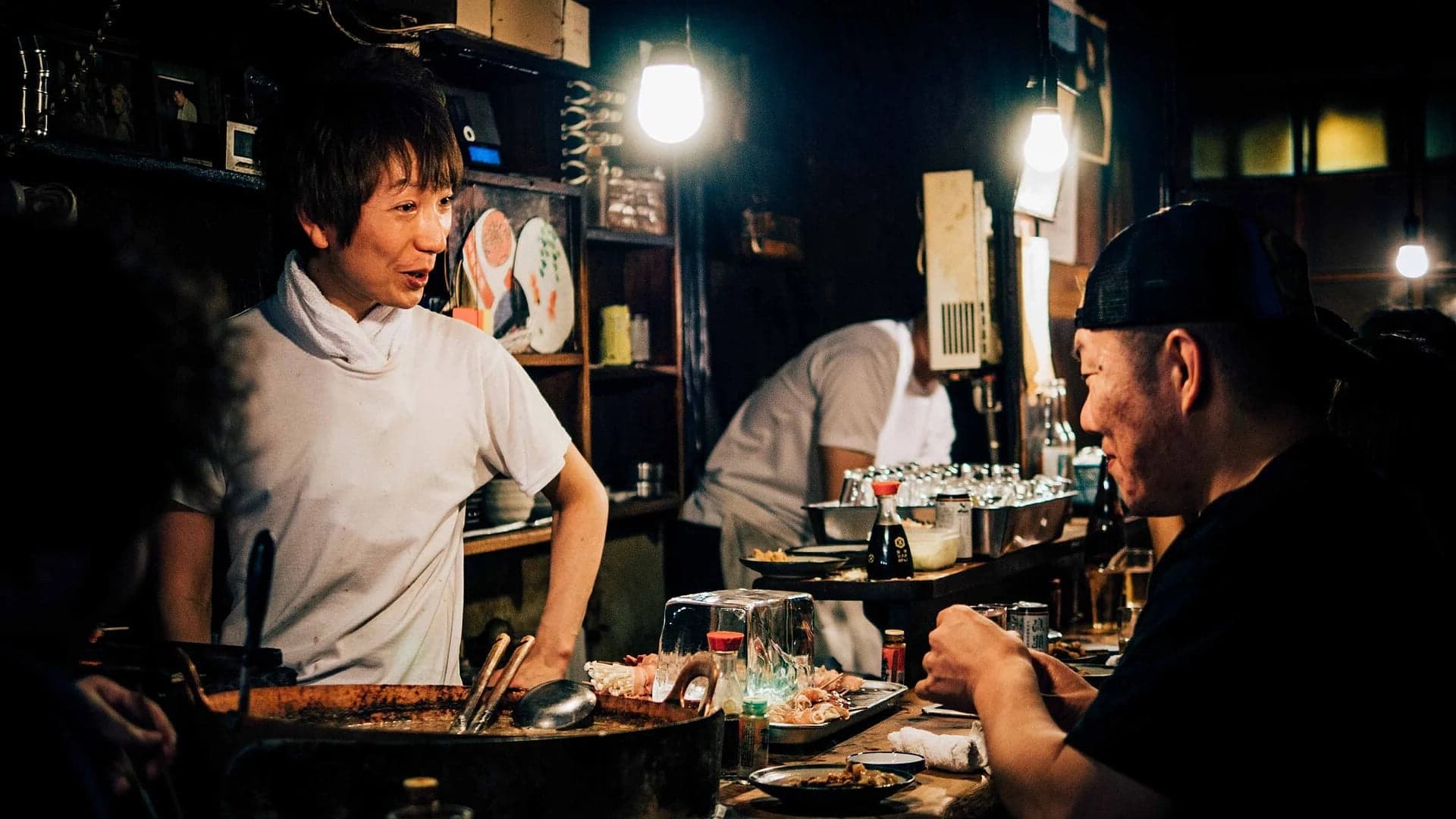 Cocinero, barra, platos y cliente en un pequeño izakaya de Tokio