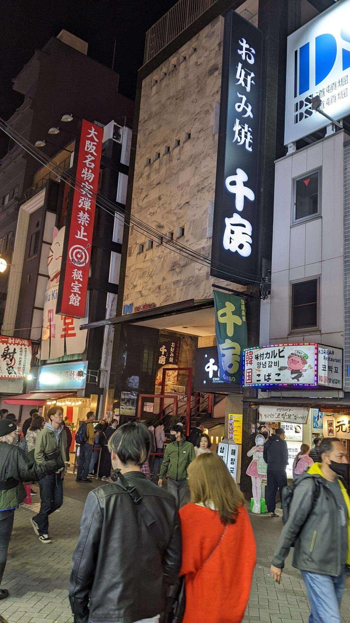 Calle concurrida frente a un restaurante de okonomiyaki en Dotonbori, Osaka