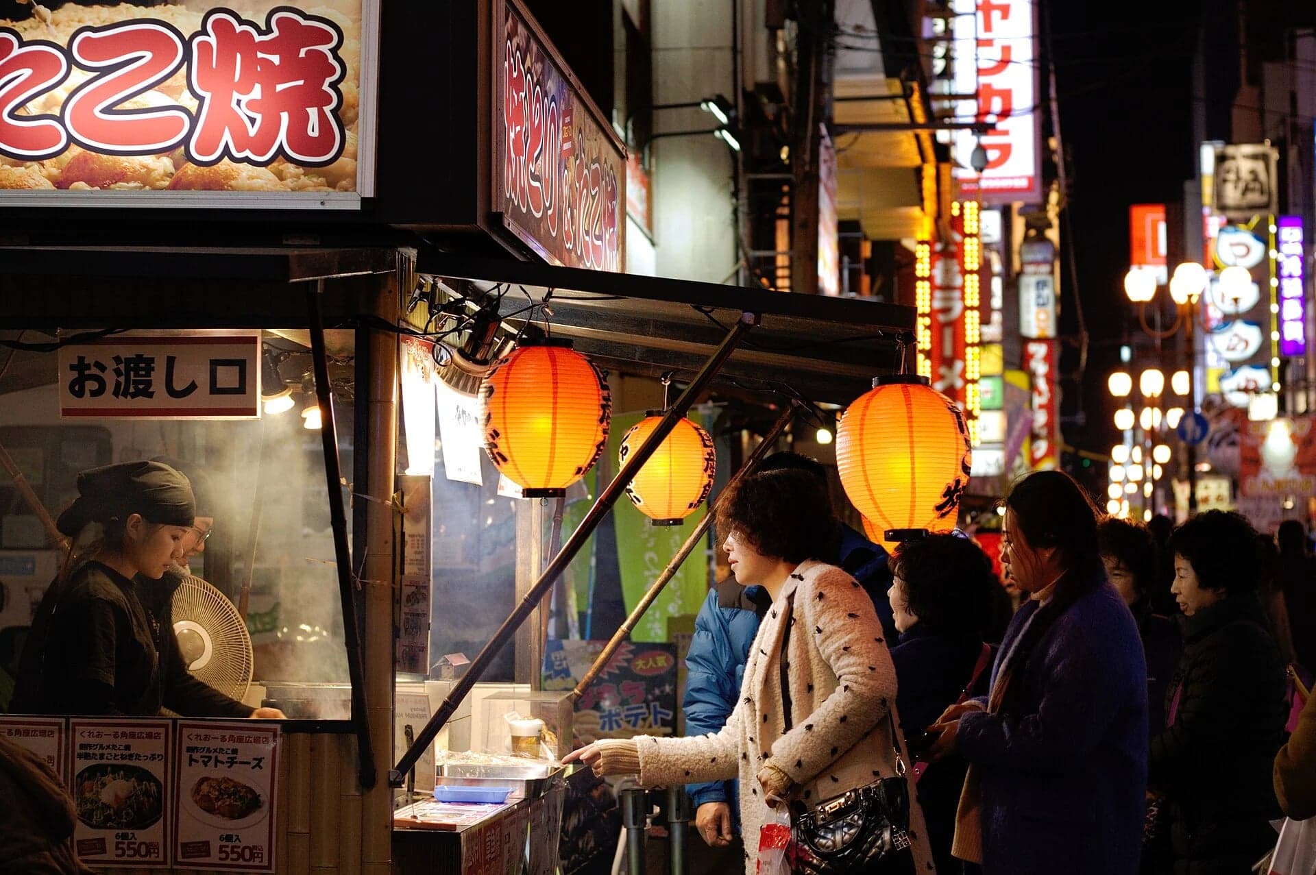 Cocinera preparando comida callejera en un puesto de Dotonbori rodeado de clientes