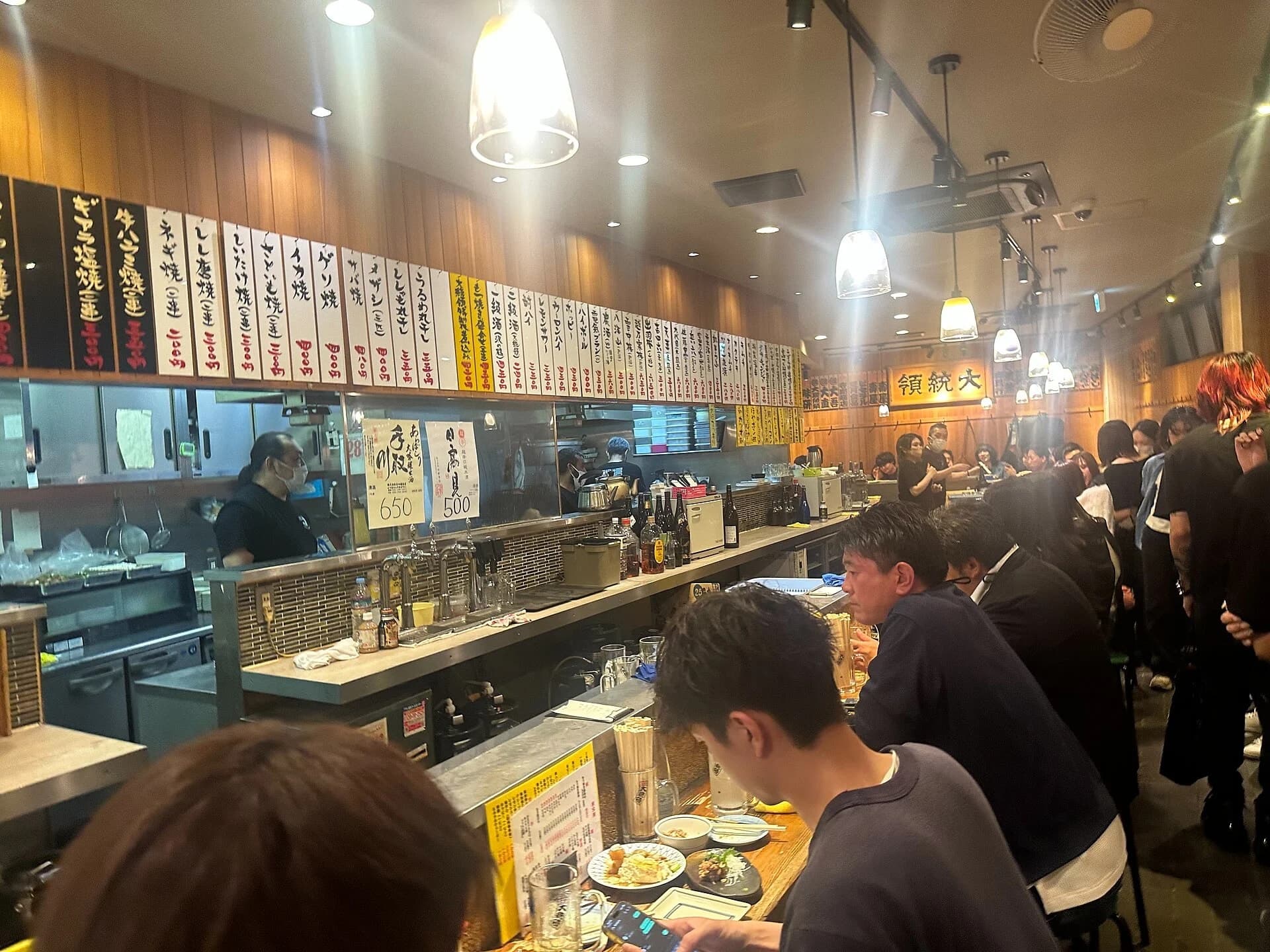 Busy Tokyo izakaya counter with food, drinks and local diners